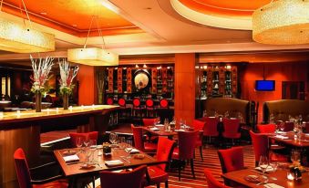 a restaurant with red chairs and tables , a bar area , and various wine bottles on display at The Ritz-Carlton, Marina del Rey