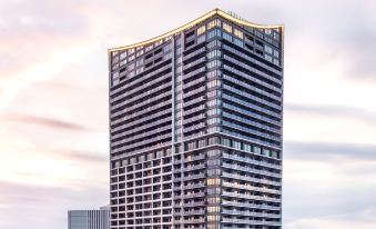 a tall , modern building with a curved design and large windows is shown against a cloudy sky at Oakwood Suites Yokohama