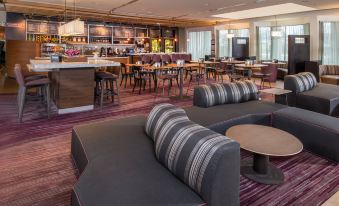 a modern lounge area with gray and black striped couches , tables , and a bar in the background at Courtyard Fairfax Fair Oaks