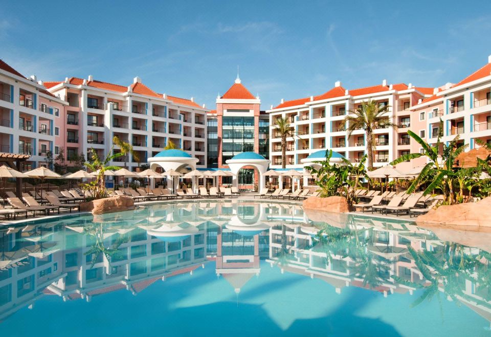 a large hotel with a pool surrounded by lounge chairs and umbrellas , providing a relaxing atmosphere at Hilton Vilamoura As Cascatas Golf Resort & Spa