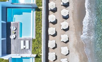 a beautiful beachfront property with multiple swimming pools , umbrellas , and lounge chairs , surrounded by lush greenery and the ocean at Grecotel LUXME White