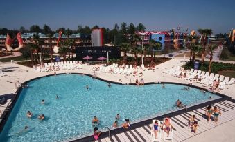 a crowded swimming pool with people enjoying the water and a hotel in the background at Disney's All-Star Music Resort