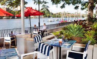 an outdoor dining area near a body of water , with several tables and chairs arranged for guests to enjoy their meal at Stamford Plaza Brisbane