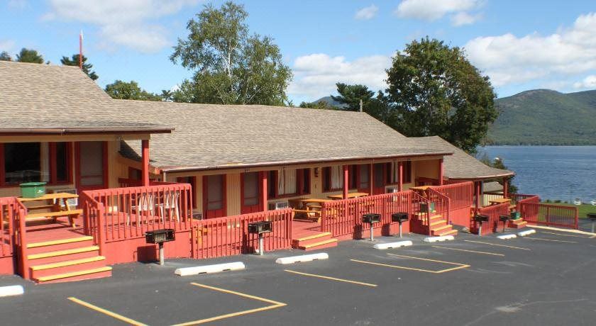 a motel with a red exterior and tan roof , surrounded by trees and parked cars at Capri Village