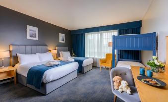 a modern hotel room with blue walls , white beddings , and yellow accents , including a bunk bed and couch at Hillgrove Hotel, Leisure & Spa