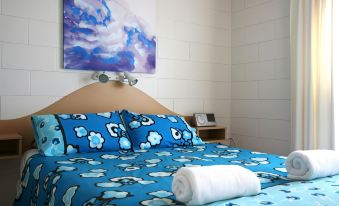 a cozy bedroom with a blue and white bedspread , a blue pillow , and a painting on the wall at Lake Edge Holiday Units