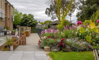 a beautiful flower garden with various flowers and plants , surrounded by a paved area and a building at Parkwood Motel & Apartments