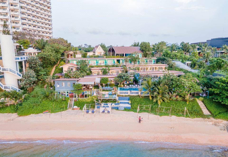 a large beach with a few people and boats , surrounded by buildings and trees , is shown from an aerial view at Pattaya Paradise Beach Resort