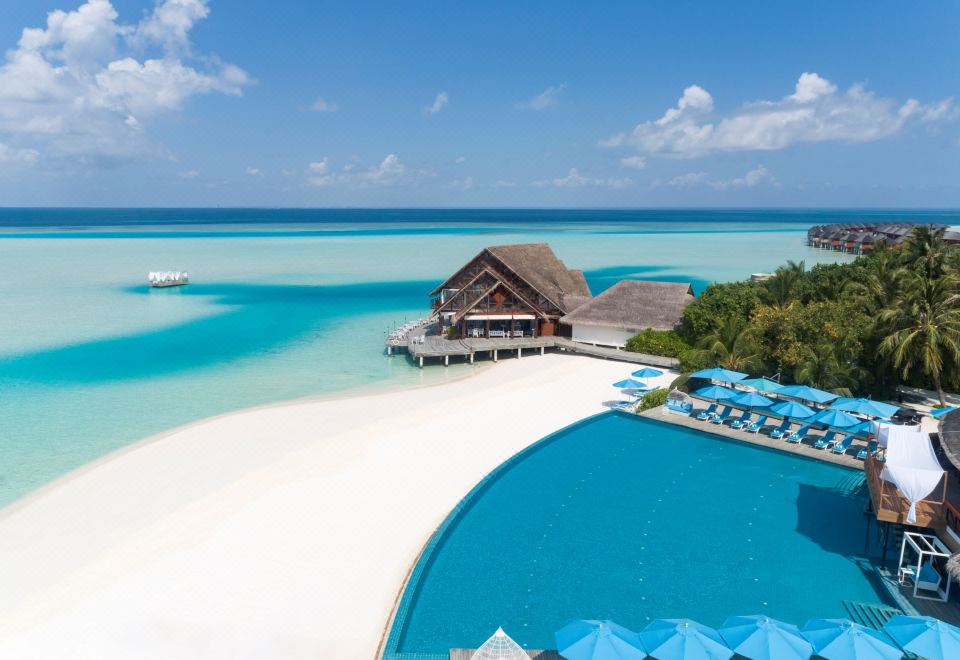 a resort with a large pool surrounded by lounge chairs and umbrellas , as well as a sandy beach in the background at Anantara Dhigu Maldives Resort