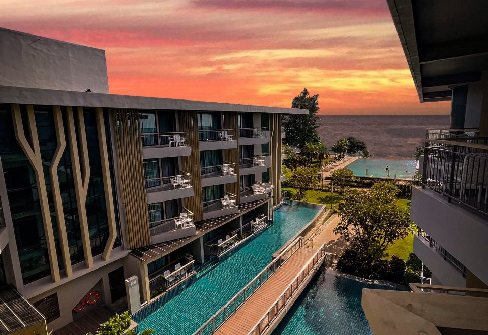 a luxurious apartment building with a swimming pool , surrounded by lush greenery and the ocean in the background at Sand Dunes Chaolao Beach Resort