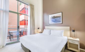 a large , white bed with a headboard is in a room with a window and a door at Oaks Sydney Goldsbrough Suites