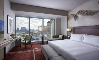 The room on an upper floor features large windows, a bed, and a desk in the middle, providing a view of the city at Studio City Hotel