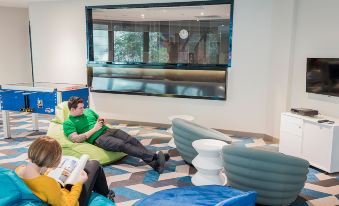 two people are sitting on bean bag chairs in a room with large windows and blue stools at Capri by Fraser Brisbane