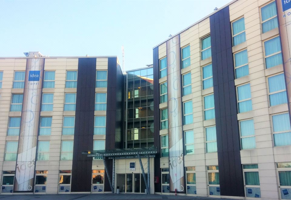 a modern office building with multiple floors and balconies , situated in front of a clear blue sky at Idea Hotel Milano Malpensa Airport