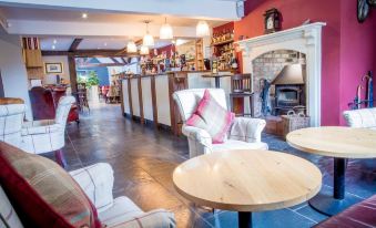 a cozy restaurant with wooden tables , white chairs , and red cushions , along with a bar area at The Nags Head