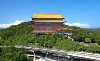 The hotel is a tall building with an elevated roof and a tower-like structure on top, situated in a city, and serves as accommodation for guests at The Grand Hotel