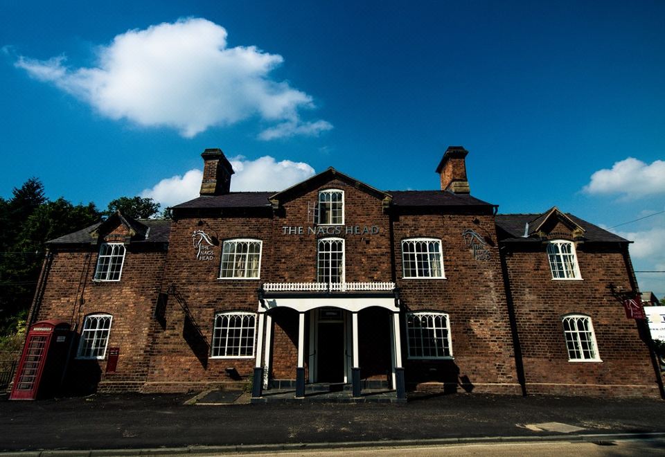 a large brick building with white columns and a blue sky in the background , surrounded by trees at The Nags Head