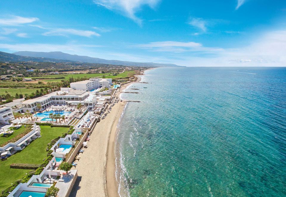 aerial view of a beautiful beach resort with multiple swimming pools , clear blue water , and lush green grass at Grecotel LUXME White