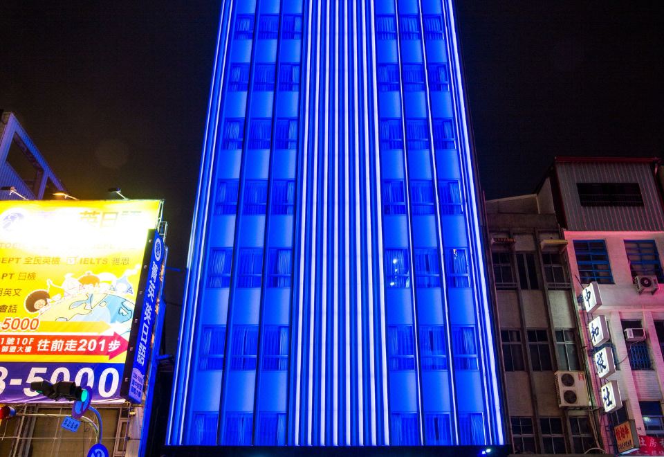 "a tall , blue skyscraper with the word "" airlines inn "" on top is lit up at night" at Airline Inn Kaohsiung Station