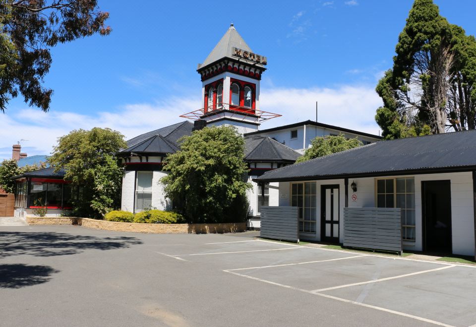 a large building with a red and white tower is surrounded by trees and has a parking lot in front of it at Hobart Tower Motel