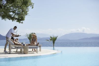 a woman is sunbathing on a lounge chair by a pool with a view of the ocean at Ikos Dassia Ikos Dassia - All Inclusive Photo