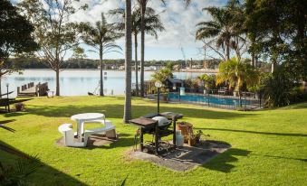 a lush green lawn with a grill set up in the middle , surrounded by palm trees and a lake at Lake Edge Holiday Units