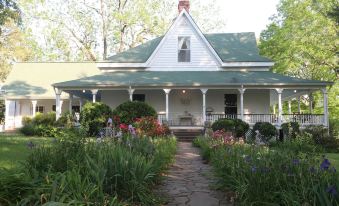 a white house with a green roof and balcony is surrounded by plants and flowers at The Stovall House