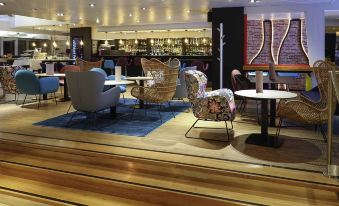 a modern lounge area with various seating options , including chairs and couches , in front of a bar at Novotel Dijon Sud