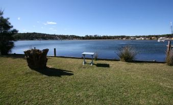 a grassy area near a body of water , with a bench and a chair placed near the water 's edge at Lake Edge Holiday Units