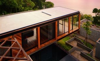 a modern house with a large glass window and wooden deck overlooking a body of water at The Naka Phuket, a member of Design Hotels