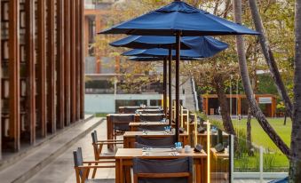 an outdoor dining area with several tables and chairs , some of which are covered with blue umbrellas at The Naka Phuket, a member of Design Hotels