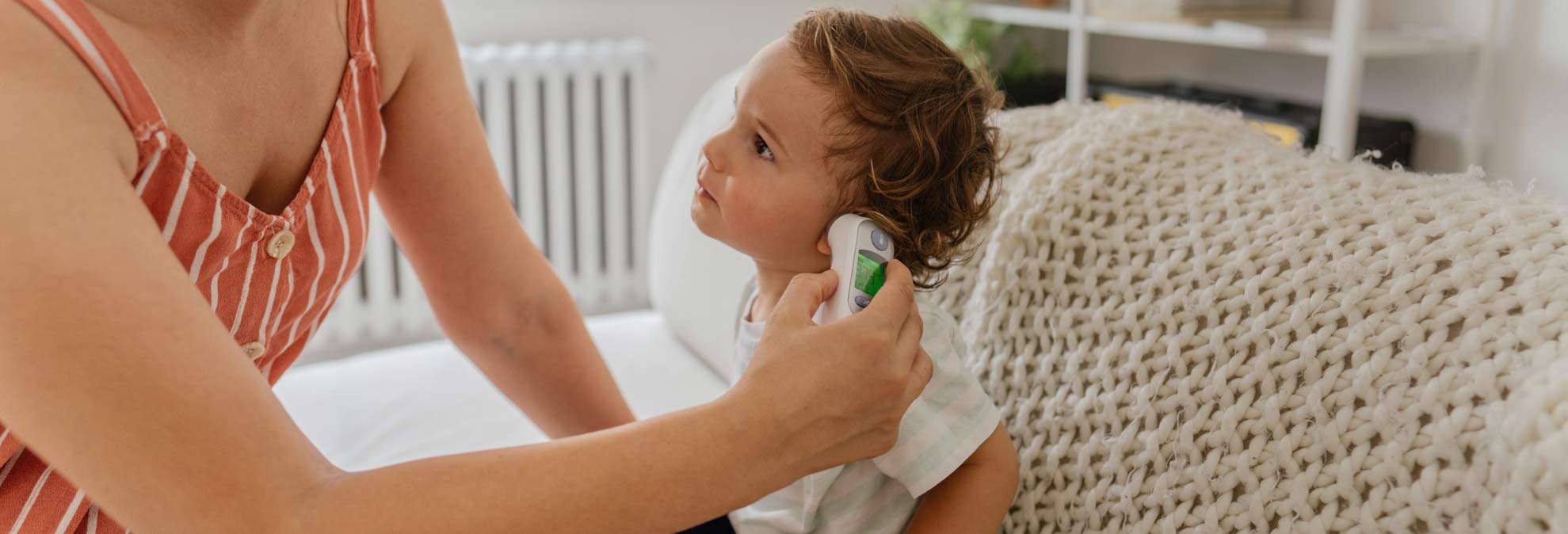 adult person checking temperature of toddler using an in-ear thermometer