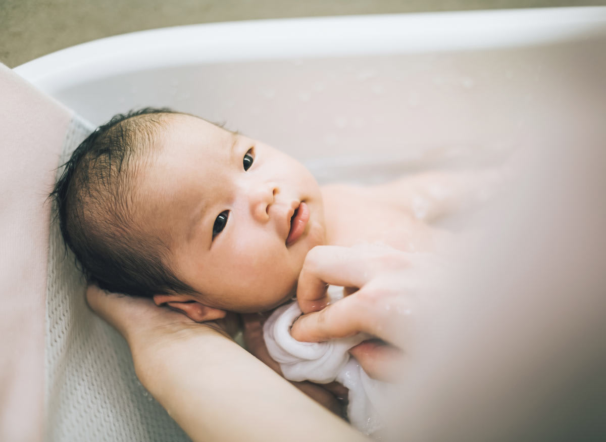 detail of baby in small tub being held by adult during a bath