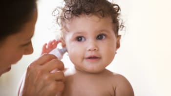 a toddler having her temperature read using an in-ear thermometer