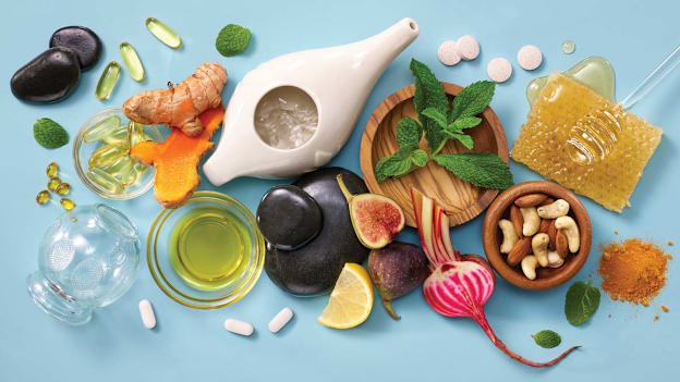 overhead view of various natural cure remedies (neti pot, honey, beets, lemons, vitamin c and d supplements, cupping glass, tumeric, mint, and massage stones)