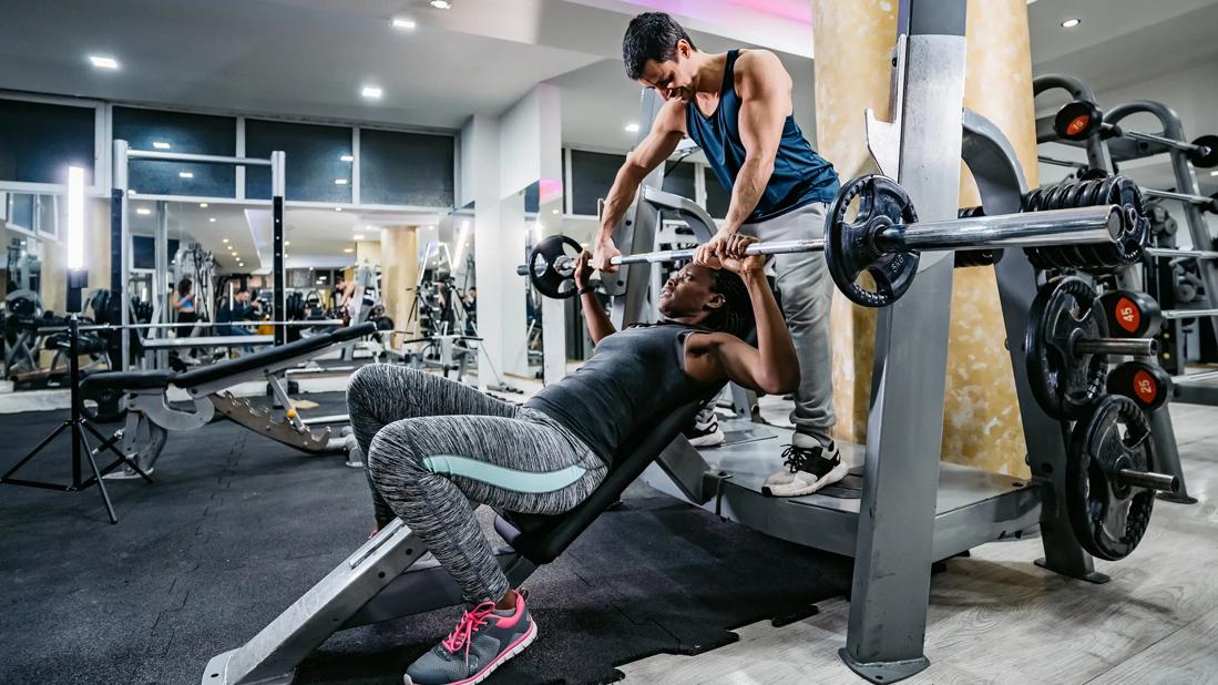 Person spotting a person doing an inclined bench press in gym