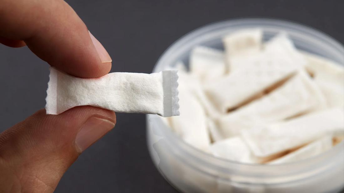 Fingers holding a nicotine pouch in front of container of nicotine pouches