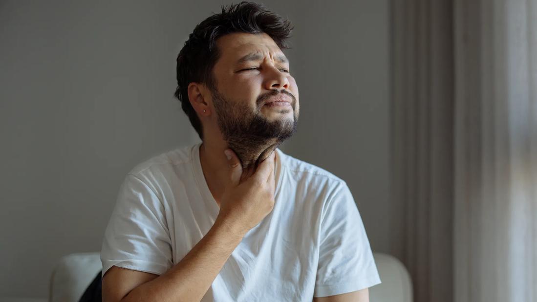 person sitting down, holding their hand to their throat