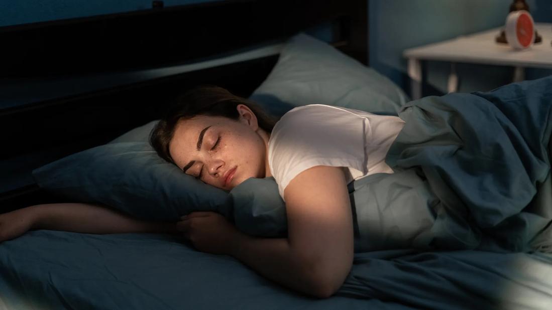 Female asleep in bed in darkened bedroom, red alarm clock on table