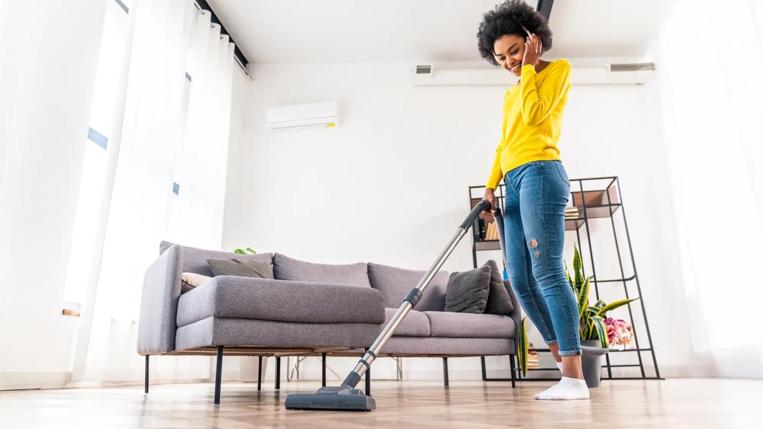 Smiling person with headphones on, sweeping floor in living room