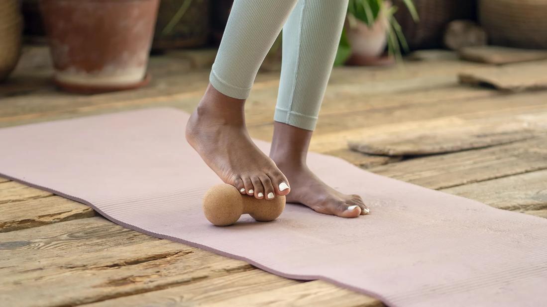 Bare feet of person standing on exercise mat, with one foot rolling on a roller