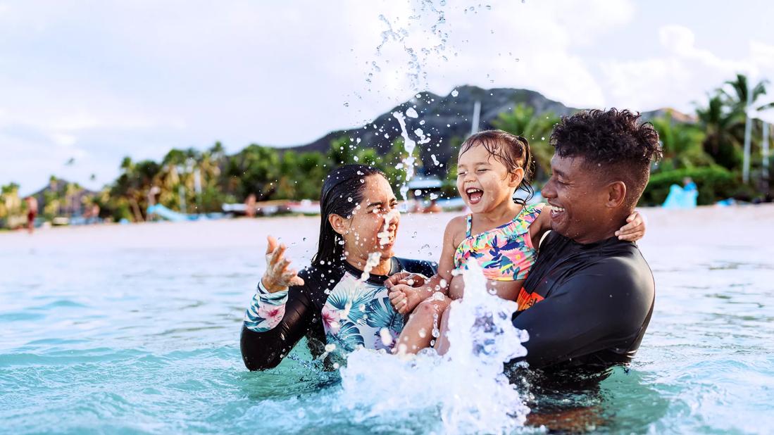 Caregivers holding toddler, playing in ocean