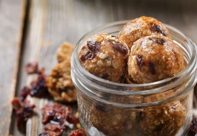 Closeup of cranberry oat peanut butter energy balls in a cup on a wooden table with ingredients in background.