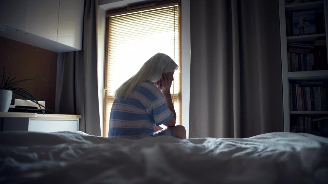 Person sitting on bed in pjs with head in hand, eyes closed