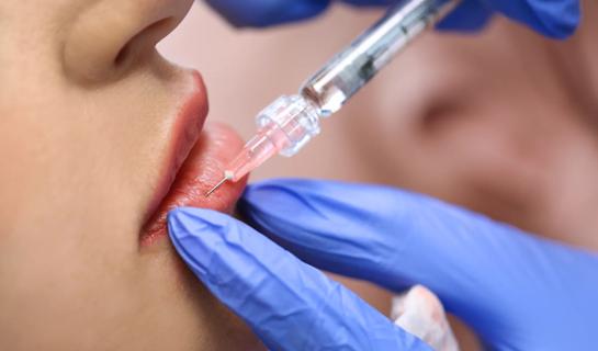 Needle being injected into lips by gloved hands