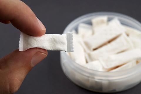 Fingers holding a nicotine pouch in front of container of nicotine pouches