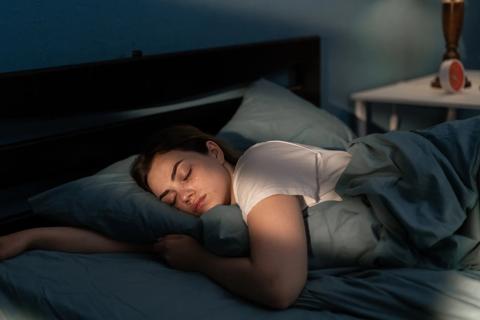 Female asleep in bed in darkened bedroom, red alarm clock on table