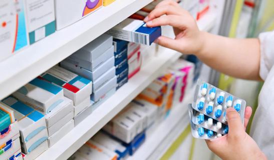 Hands selecting medicine from shelves of medicines