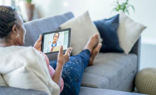 Female reclining on couch holding laptop, having video appointment with healthcare provider