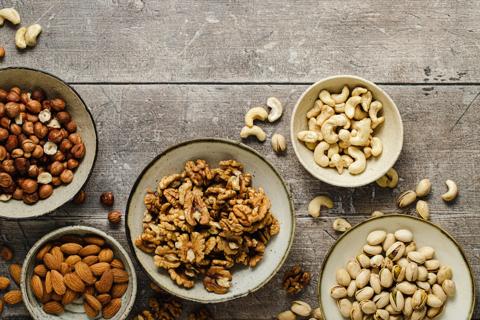 Separate bowls of shelled almonds, walnuts, cashews, hazelnuts, and in-shell pistachios